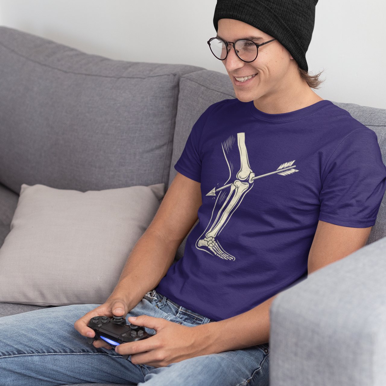 Gamer wearing purple arrow-to-the-knee shirt while holding controller and smiling on couch