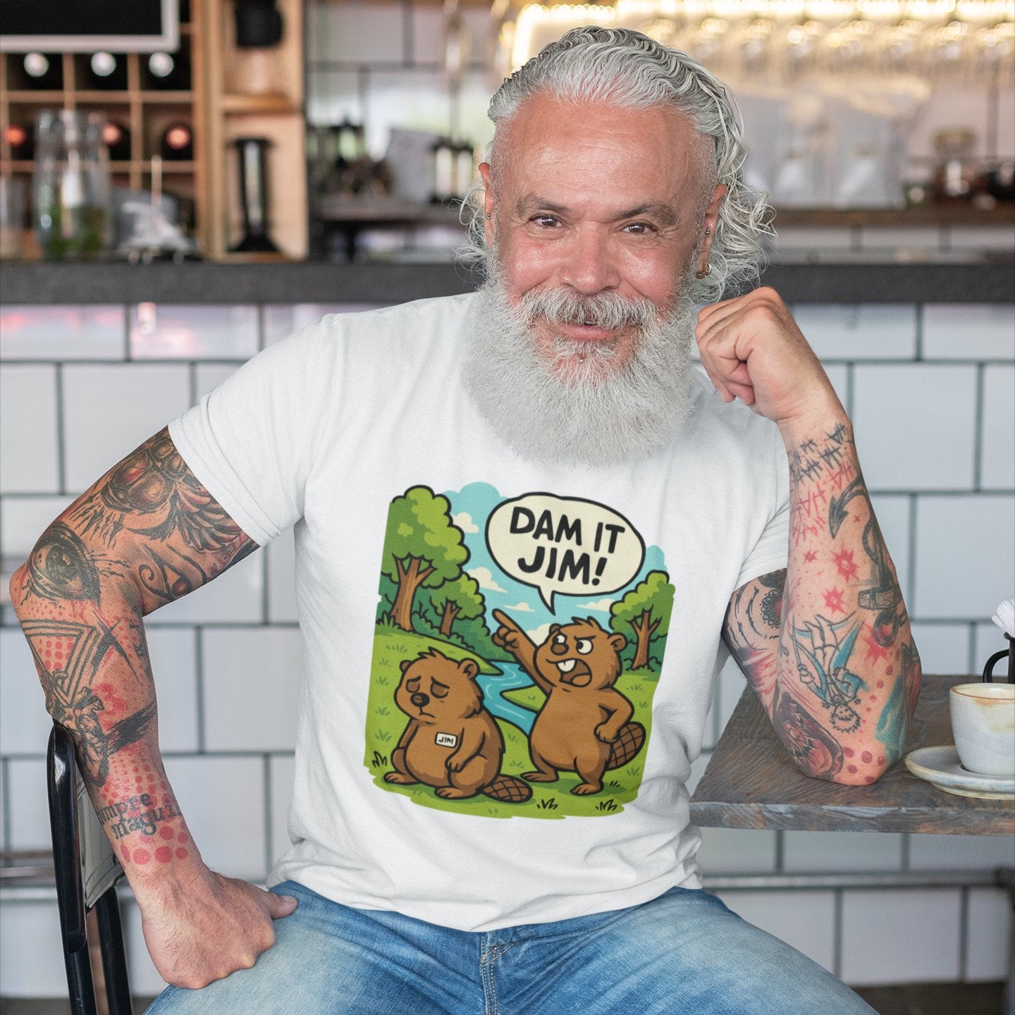 Man wearing funny beaver t-shirt with “Dam It Jim!” design, seated in a casual, relaxed setting.
