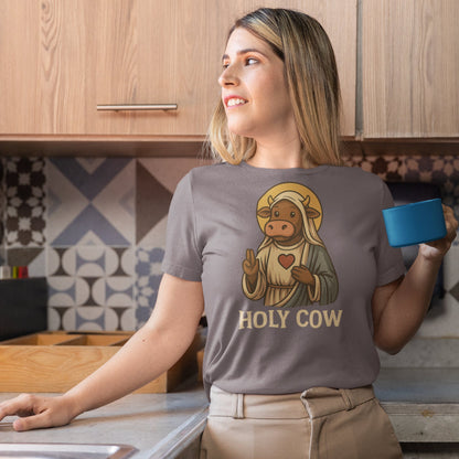 Woman in kitchen wearing grey “Holy Cow” pun t-shirt featuring illustrated cow saint with robe and halo
