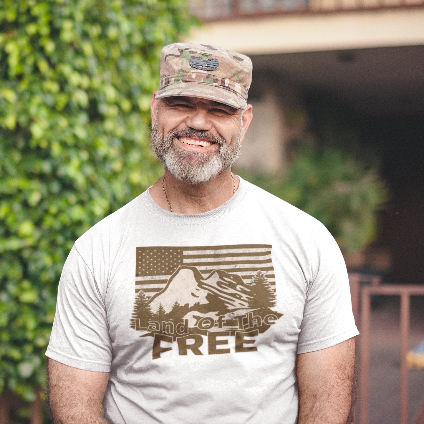 Man wearing “Land of the Free” t-shirt with mountain graphic and American flag design in natural outdoor setting.