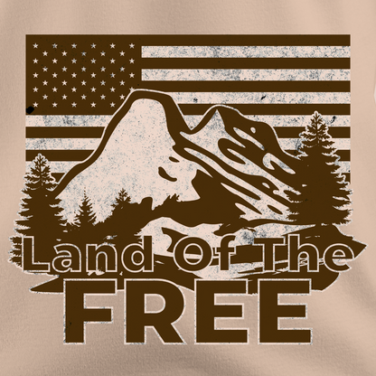 Close-up of vintage “Land of the Free” t-shirt design with mountain, pine trees, and American flag background in a rustic, outdoorsy style.